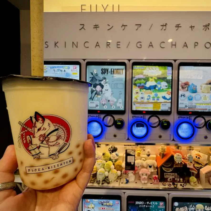 image of bubble tea in hand at front in frame, with japanese toys and figurine vending machine in the background